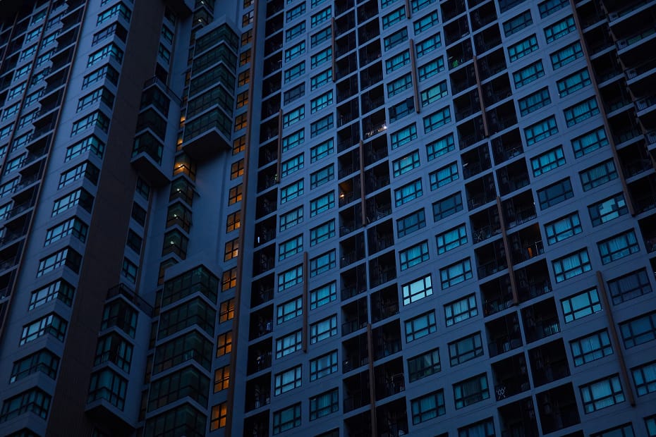 A imagem retrata a fachada de um condomínio moderno à noite, com luzes acesas em algumas janelas, simbolizando a dinâmica da vida urbana. A gestão condomínio eficiente é essencial para manter a organização, segurança e conforto dos moradores em empreendimentos desse porte.
