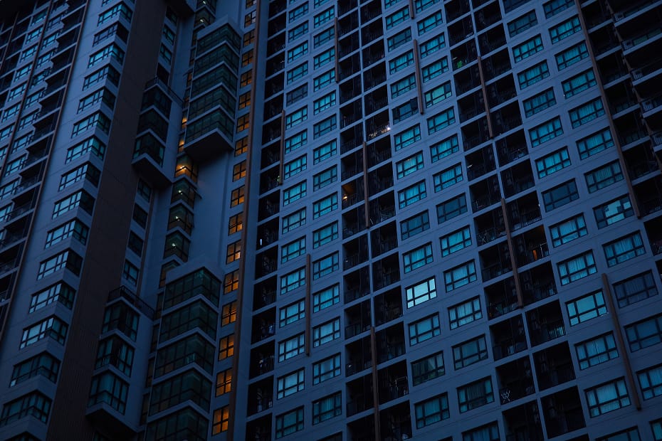 A imagem retrata a fachada de um condomínio moderno à noite, com luzes acesas em algumas janelas, simbolizando a dinâmica da vida urbana. A gestão condomínio eficiente é essencial para manter a organização, segurança e conforto dos moradores em empreendimentos desse porte.